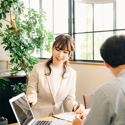 ビジネススーツを着た女性がお客様を相手に右手を差し出し説明している様子のイメージ画像